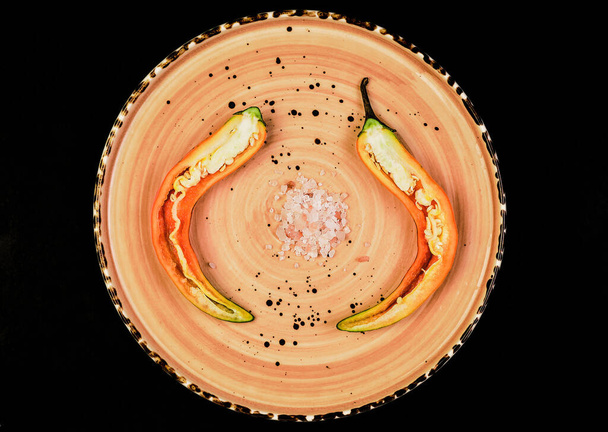 Peperoni messicani piccanti, tagliati a metà su un piatto con sale. jalapeno - tapas spagnole su sfondo di pietra nera. Focus selettivo, vista dall'alto piatta, concetto di natura morta alimentare - Foto, immagini