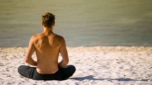 Sitting man doing yoga on shore of ocean - Foto, imagen