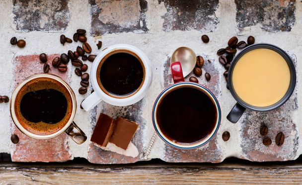 Birkaç fincan espresso, tuğla pencere pervazında rigerto ve mocha. Sıcak kahvenin, çikolata dilimlerinin ve kahve tanelerinin üst görüntüsü. Arkaplan fikri - Fotoğraf, Görsel