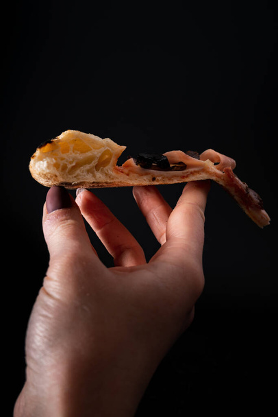A closeup shot of a tasty looking pizza in a person hand isolated on a black background - Foto, afbeelding