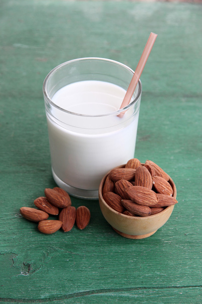 Almond milk in glass with almonds in bowl, on color wooden background - Foto, immagini