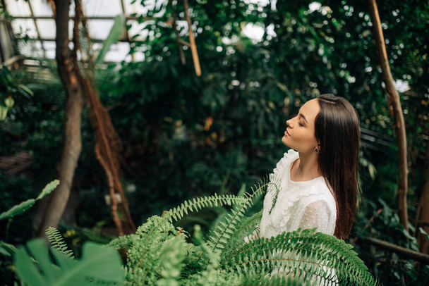Young woman relaxes and enjoys inside orangery among green tropical plants. - Fotó, kép