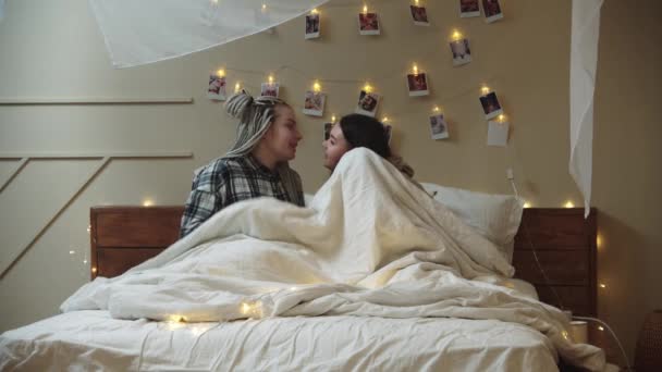 Twee jonge vrouwen liggen op bed en bedekken zich met een deken met hun hoofd - Video