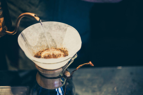 A closeup shot of water pouring into a coffee filter with ground bits over a glass pot - Zdjęcie, obraz