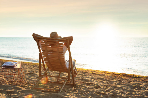 Man relaxing on deck chair at sandy beach. Summer vacation - Fotografie, Obrázek