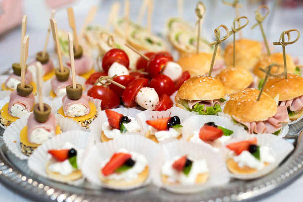 The buffet at the reception. Assortment of canapes on a table. Banquet service. Catering food, snacks with different types of cheese, ham, salami, prosciutto, shrimp, vegetables and fruits. Party Concept.The buffet at the reception. Assortment of can - Photo, Image