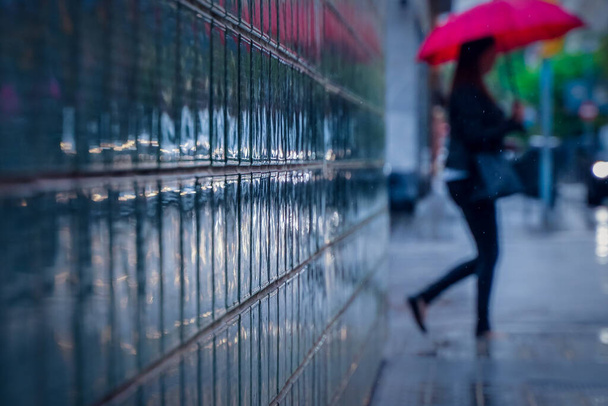 Um tiro de foco seletivo de um edifício de vidro com uma mulher com um guarda-chuva andando no fundo - Foto, Imagem