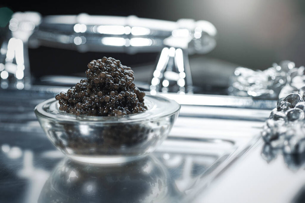Black caviar. Black sturgeon caviar in a glass bowl on a silver tray - Photo, Image