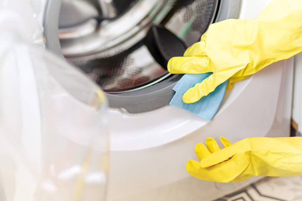 Kéz a kézben védőkesztyű óvatosan tisztítsa meg a mosógép. Rendszeres takarítás. A szobalány takarít. - Fotó, kép