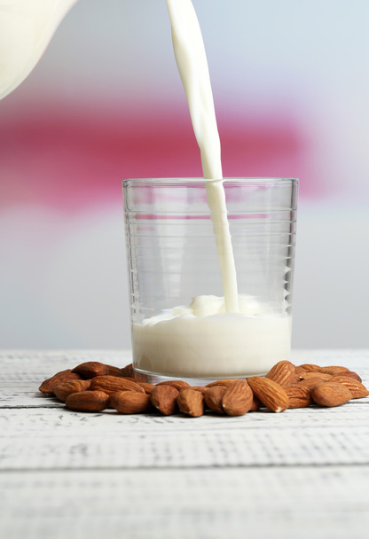 Almond milk is poured into glass, on color wooden table, on light background - Фото, зображення