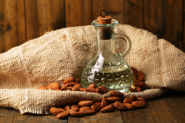 Bottle with almonds oil on color wooden background - Photo, image