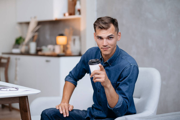 smiling young man with a Cup of coffee pointing at you . - Photo, Image