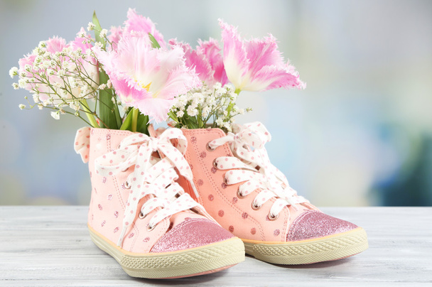 Beautiful gumshoes with flowers inside on wooden table, on bright background - Foto, Imagen