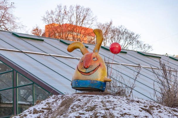 Huge funny plastic rabbit with ears and a balloon in the bushes against the blue sky - Photo, Image