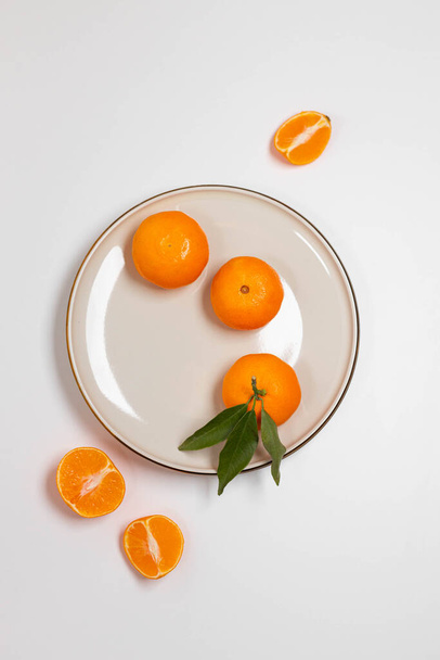 Frutas frescas de mandarina o clementina en un plato beige con un borde de oro sobre la mesa. Fondo de fruta de colores. Piso tendido, vista superior, espacio para copiar. Composición decorativa navideña - Foto, Imagen
