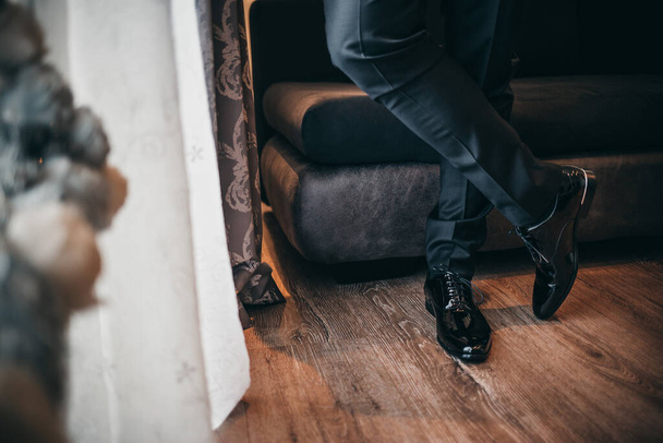 A person wearing a pair of polished jet black Oxford shoes and standing with crossed legs - 写真・画像