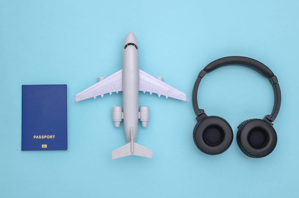 Mavi arka planda müzik kulaklığı ve pasaportu olan oyuncak bir uçak. Seyahat konsepti. Düz yatıyordu. Üst görünüm - Fotoğraf, Görsel