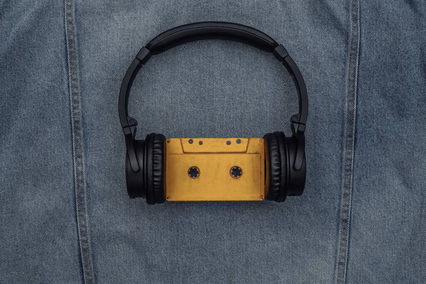 Zwarte stereo hoofdtelefoon met audiocassette op een blauwe jeans achtergrond. - Foto, afbeelding