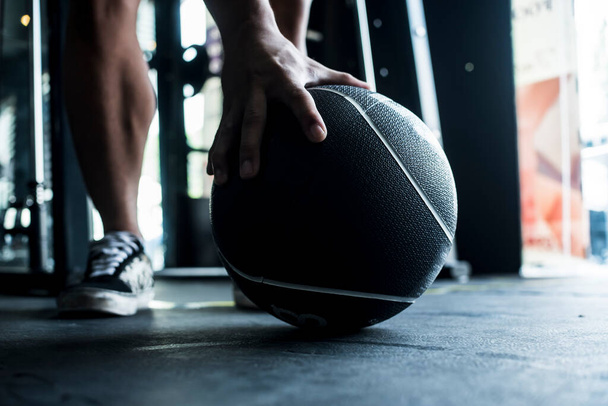 A medicine ball on the rubber floor of a gym is grabbed by an unidentified person. Workout and training concept. - Photo, image