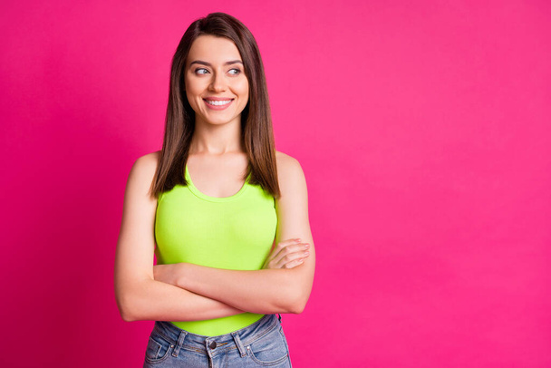 Photo of lovely young girl folded arms look side empty space shiny smile wear green top isolated bright pink color background - Zdjęcie, obraz