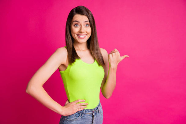 Photo of excited young girl indicate thumb empty space shiny toothy smile wear green top isolated vivid pink color background - Foto, afbeelding