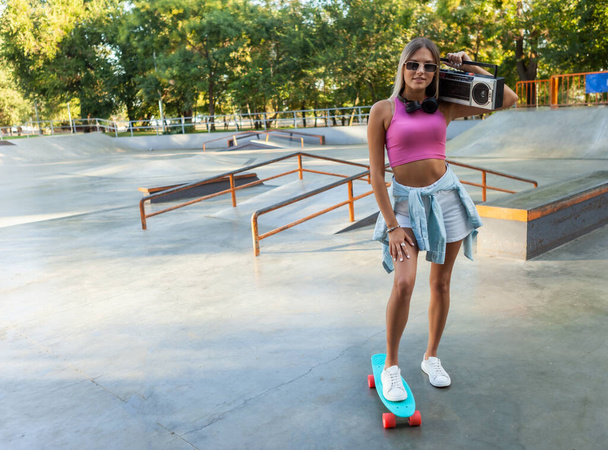 Obraz młodej stylowej kobiety łyżwiarki z krążownikiem i magnetofonem retro boombox w skateparku - Zdjęcie, obraz