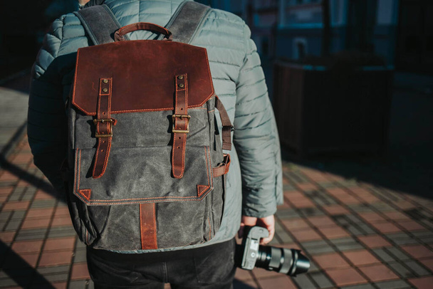 A selective focus shot of a male wearing a backpack and holding a camera while walking on the street - Foto, Imagem