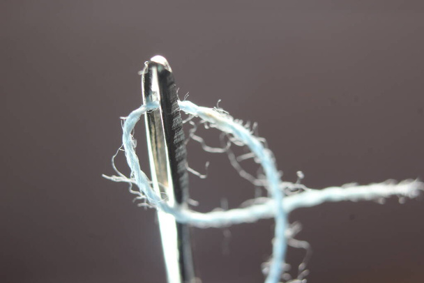 Fotografia macro da agulha de costura. Agulha pequena com fio no ilhó, isolada sobre o fundo preto. - Foto, Imagem