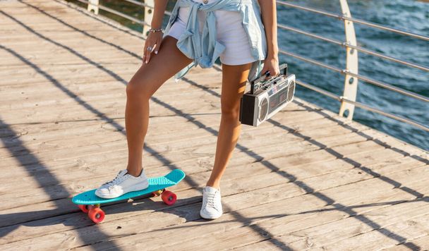 Nuori nainen skeetboard ja retro nauhuri rannalla kirkas aurinkoinen päivä - Valokuva, kuva