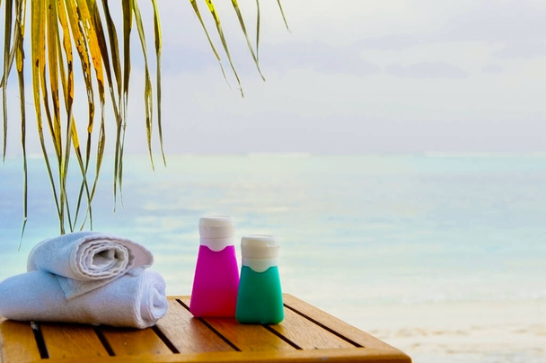 Sun cream bottles with white rolled towels on the sea shore view. Beach accessories outdoors - Photo, Image