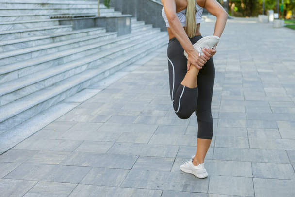 Nuori hoikka kunto nainen urheiluvaatteet tekee venyttely ja lämmittely harjoituksia jalka ennen harjoittelua ulkona - Valokuva, kuva
