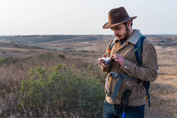 A Caucasian hiker man with a beard, wearing a brown jacket, backpack, taking a picture of the field - Photo, image