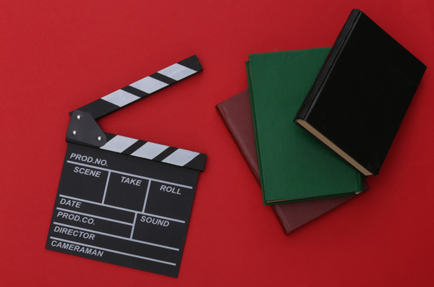 Film clapper board and books on red background. Movie by book. Cinema industry, entertainment. Top view - Zdjęcie, obraz