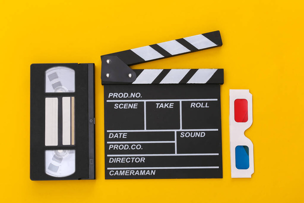 Tablero de aplausos de película, gafas 3d, casete de vídeo sobre fondo amarillo. Vista superior - Foto, imagen