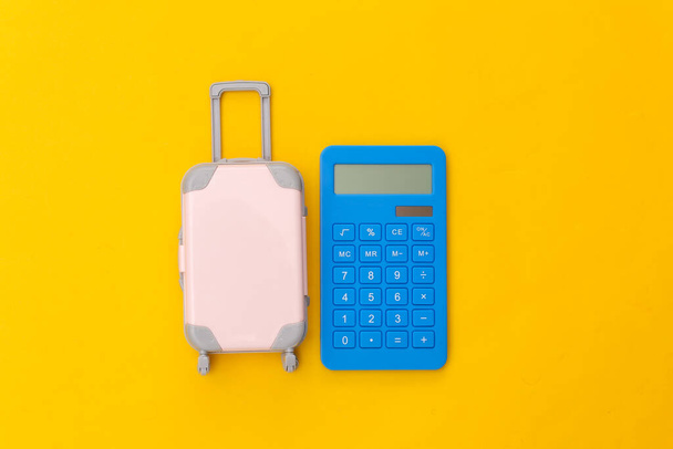 交通費だ。黄色の背景に電卓付きミニプラスチック旅行スーツケース。最上階だ。平敷 - 写真・画像