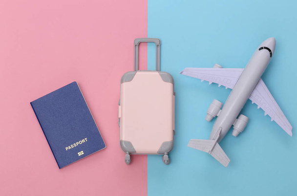 Lentomatkustus tasainen lay. Mini muovi matkalaukku, passi ja lentokone vaaleanpunainen sininen pastelli tausta. Yläkuva. - Valokuva, kuva