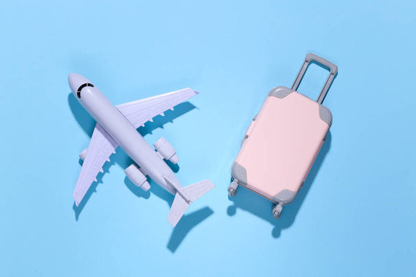 Minimalisme de voyage. Mini valise de voyage en plastique, globe et avion sur fond bleu avec ombre profonde. Style minimal. Vue de dessus, plan plat - Photo, image