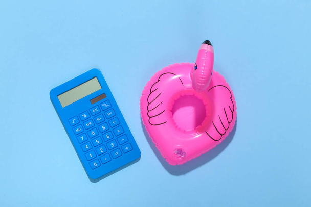 Надувной розовый фламинго с калькулятором на синем солнечном фоне. Летние каникулы. Минимализм. Вид сверху. - Фото, изображение