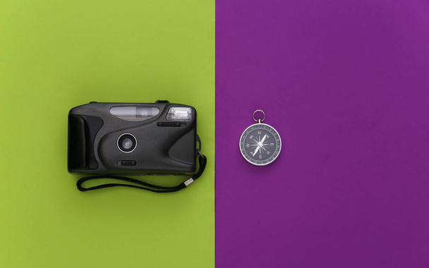Viagem minimalismo, aventura flat lay. Bússola e câmera em fundo verde roxo. Vista superior - Foto, Imagem