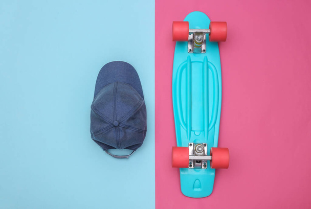 Flat lay composition of mini cruiser board and cap on pink blue background. Youth, hipster accessories. Top view - Zdjęcie, obraz