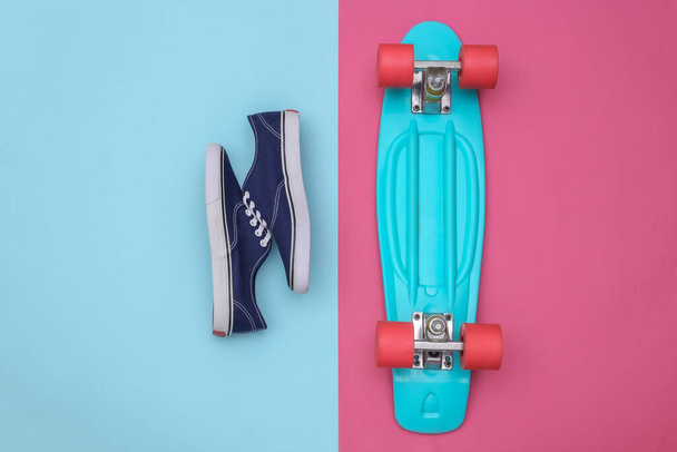 Flat lay composition of mini cruiser board, sneakers on pink blue background. Youth, hipster outfit. Top view - Photo, Image