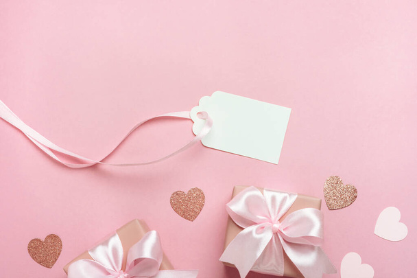 Confezioni regalo con nastro rosa e cuori su sfondo rosa pastello. Composizione di San Valentino con tag regalo vuoto. Vista dall'alto, posizione piatta con spazio libero per il testo. - Foto, immagini