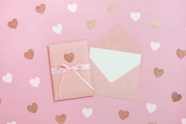 Pembe kurdeleli hediye paketi ve kalpli pastel pembe arka planda boş bir kartın olduğu zarf. Sevgililer Günü kompozisyonu ve yazı için boş yeri var. Üst manzara, düz uzanma. - Fotoğraf, Görsel