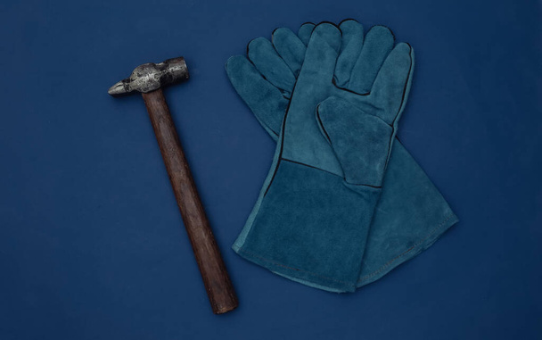 Arbeitshandschuhe und Hammer auf blauem Hintergrund. Ansicht von oben - Foto, Bild
