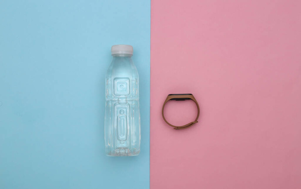 Fitness, sports minimalistic flat lay. Water bottle and smart bracelet on a blue-pink background. Top view - Photo, image