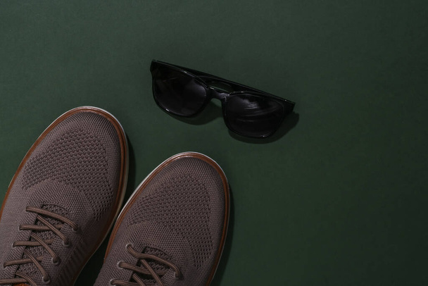 Ανδρικά παπούτσια και γυαλιά ηλίου σε πράσινο φόντο. Άνω όψη - Φωτογραφία, εικόνα