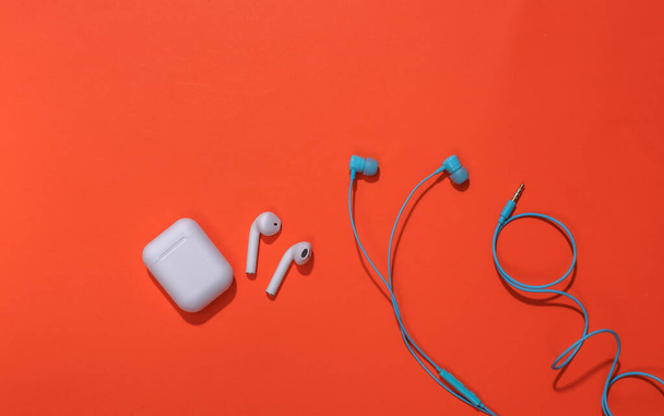 Bezdrátové sluchátka s nabíjecím pouzdrem a klasickými drátovými sluchátky na jasně oranžovém pozadí - Fotografie, Obrázek