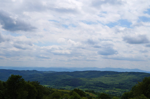 Панорамний вид на гори, вкриті зеленою травою і хвойними лісами під блакитним небом в літній день
 - Фото, зображення