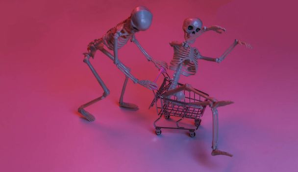 Scary funny skeletons with shopping trolley in pink blue gradient neon light - Photo, Image