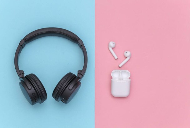 Ασύρματα μεγάλα στερεοφωνικά ακουστικά και μικρά ακουστικά με θήκη φορτιστή σε ροζ μπλε παστέλ φόντο. Άνω όψη - Φωτογραφία, εικόνα